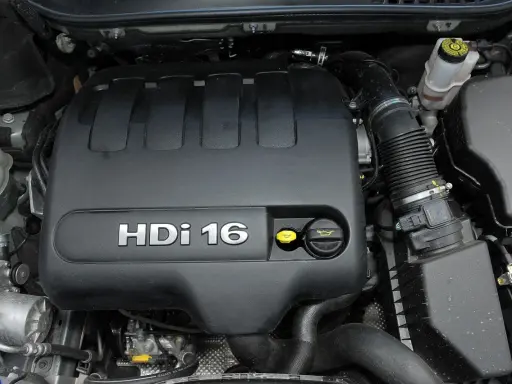 Silnik 2.0 HDi w Peugeot Expert. Widoczny czarny plastikowy dekiel z napisem HDi 16, żółty korek oleju i inne elementy komory silnika.