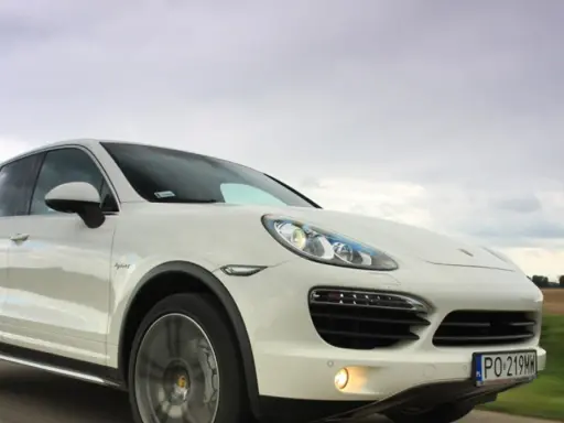 Biały Porsche Cayenne 2025 pędzi po drodze, chmury na niebie sugerują dynamiczną podróż.