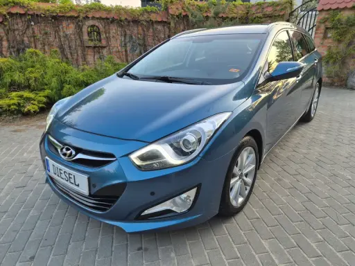 Niebieski Hyundai i40 1.7 CRDi na podjeździe z kostki brukowej, z tyłu ceglany mur porośnięty bluszczem.