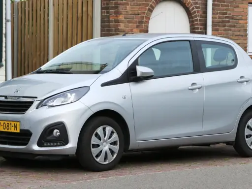 Srebrny Peugeot 108 stoi zaparkowany przed ceglanym domem.