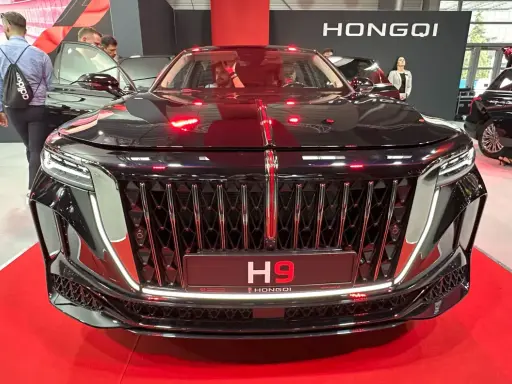 Elegancki czarny Hongqi H9 z chromowanym grillem i czerwonymi akcentami. Zainteresowani sprawdzają jego cenę na wystawie.