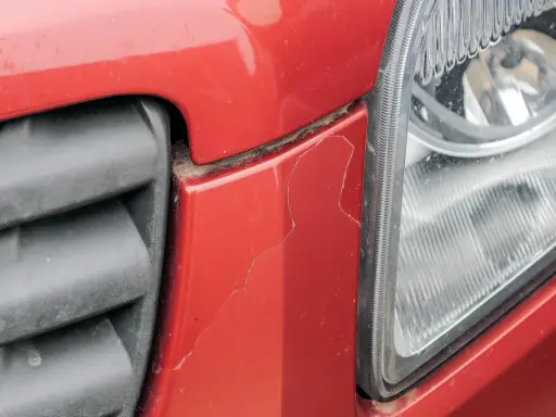 Pęknięty czerwony zderzak obok reflektora. Czas sprawdzić malowanie zderzaka cena.