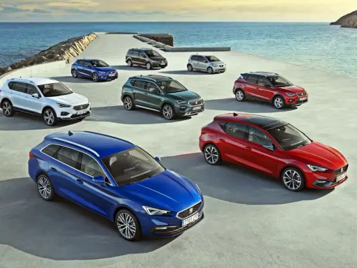 Różnorodne modele SEAT stojące nad morzem. Wśród nich biały SUV, niebieski kombi i czerwony hatchback.