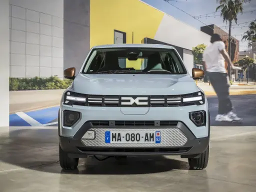 Jasnoszary dacia elektryk z miedzianymi lusterkami. Z przodu logo Dacia i tablica rejestracyjna MA-080-AM 92.
