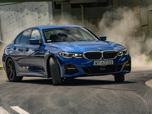 Niebieskie BMW 320i w zakręcie, unosząc tumany kurzu. Dynamiczna jazda na torze.