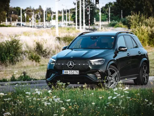 Czarny Mercedes GLE 350 z czerwonym wnętrzem zaparkowany na tle łąki i torów kolejowych.