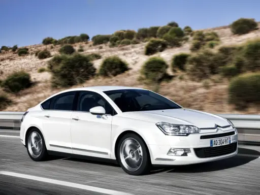 Biały Citroen C5 2.0 HDI pędzi po pustej drodze, otoczony suchymi, pagórkowatymi krajobrazami.