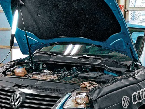 Pod maską niebieskiego VW z silnikiem 2.0 TDI, mechanik oświetla silnik lampą.