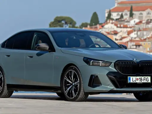 Szary BMW 520 z czarnymi felgami stoi na tle malowniczego nadmorskiego miasteczka.