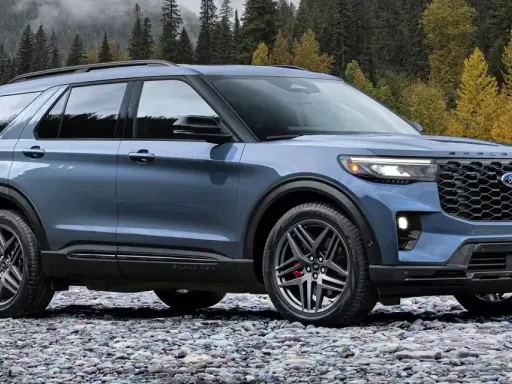 Niebieski Ford Explorer ST zaparkowany na kamienistej plaży, z jesiennym lasem w tle.