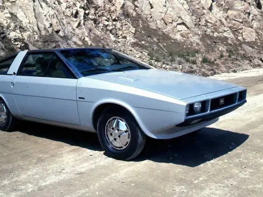 Srebrny Hyundai Pony z lat 70. na drodze w skalistym terenie.