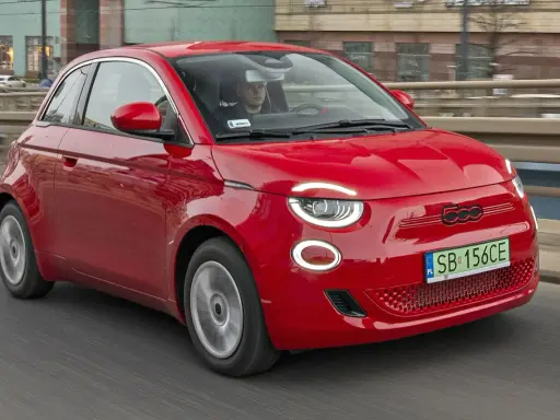 Czerwony Fiat 500 jedzie po drodze. Sprawdź aktualną fiat 500 cena i dowiedz się więcej o tym stylowym samochodzie.