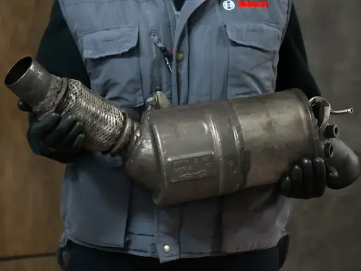 Mechanik w rękawiczkach trzyma zużyty fap, element układu wydechowego.