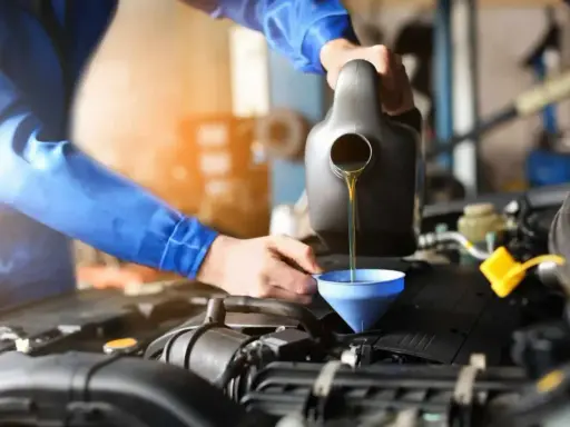 Mechanik w niebieskim kombinezonie nalewa olej do silnika przez lejek. Szybka wymiana oleju to klucz do sprawnego działania auta.