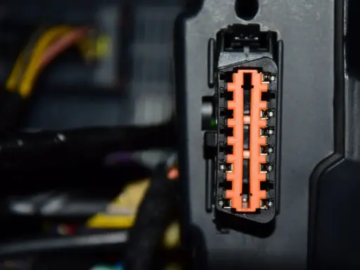 Pomarańczowe złącze elektryczne w samochodzie Mercedes B180, otoczone przewodami.