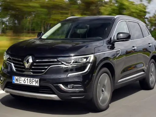 Czarny Renault Koleos 2.0 dCi pędzi po drodze, otoczony rozmytym zielonym krajobrazem.