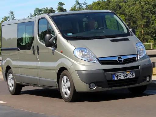 Srebrny Opel Vivaro 2.0 CDTI z przyciemnianymi szybami jedzie po drodze, otoczony zielenią.