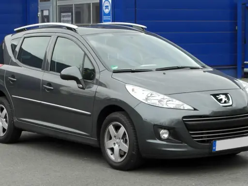 Szary Peugeot 207 1.4 benzyna z relingami dachowymi, zaparkowany przed niebieskim budynkiem.