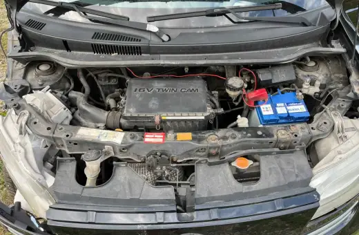 Silnik 1.6 VVT-i w Daihatsu Materia, z widocznym akumulatorem Varta i elementami układu chłodzenia.