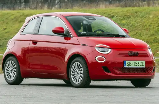 Czerwony fiat elektryczny 500 zaparkowany na tle zielonego wzgórza.