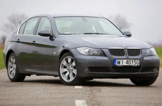 Szary sedan BMW E90 2.0 benzyna na drodze.