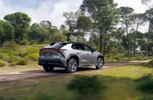 Srebrny Toyota bz4x jedzie po leśnej drodze, otoczony zielenią i drzewami.