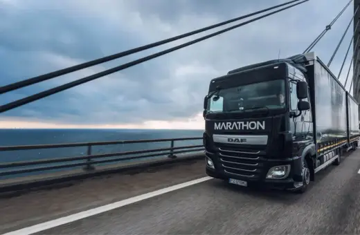 Ciężarówka DAF Marathon z silnikiem euro 6 jedzie po moście nad morzem, w tle widać farmę wiatrową.