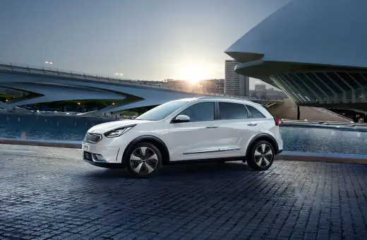 Biały Kia Niro Hybrid zaparkowany przy nowoczesnym budynku i wodzie.