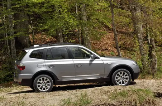 Srebrne BMW X3 E83 na leśnej ścieżce, gotowe na przygodę wśród drzew.