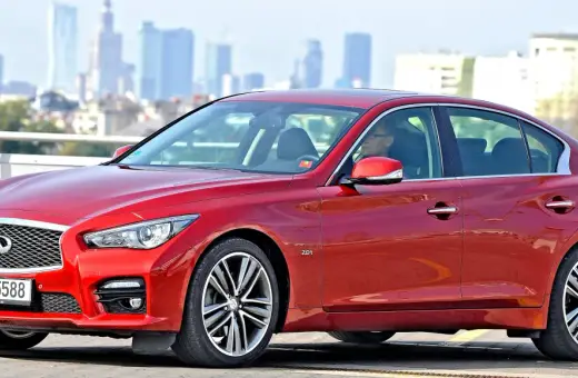 Czerwone infiniti auto z kierowcą na tle miejskiej panoramy.