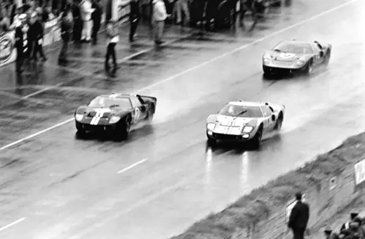 Trzy samochody Ford GT40 ścigają się po mokrym torze.