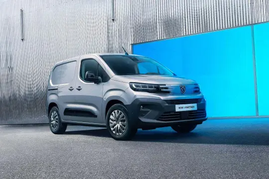 Nowy Peugeot Partner, srebrny van, stoi przed błyszczącą, falistą ścianą i jaskrawoniebieskim panelem.