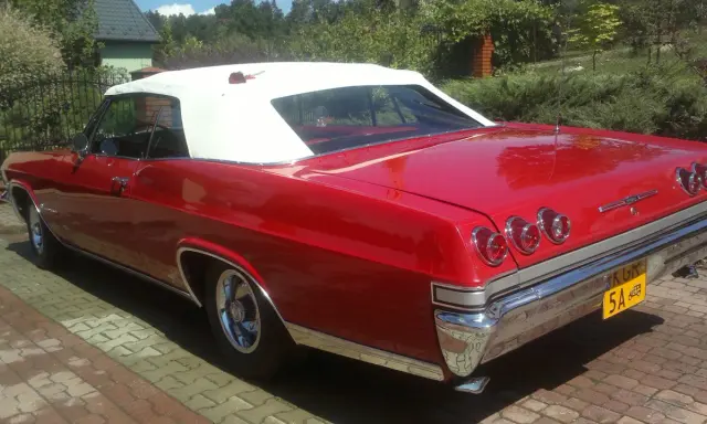 Czerwona kabrioletowa Chevy Impala z białym dachem, zaparkowana na podjeździe z kostki brukowej.