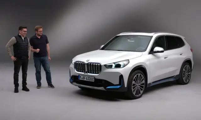 Dwóch mężczyzn stoi obok białego BMW iX1.