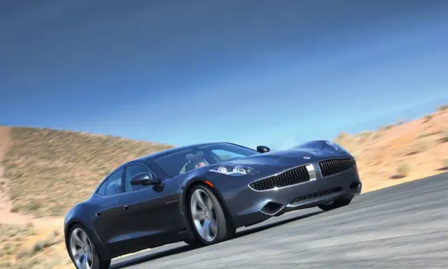 Elegancki, ciemnoszary Fisker Karma sunie po pustynnej drodze pod błękitnym niebem.