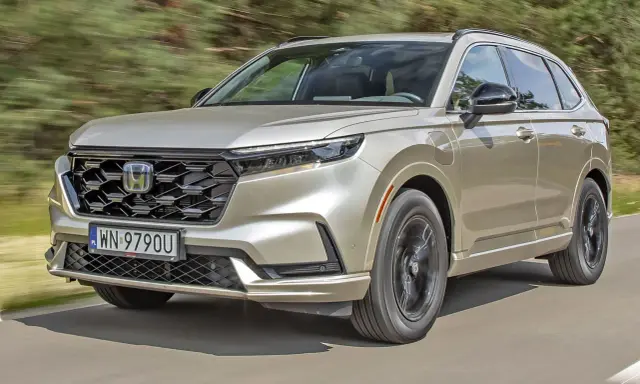 Nowy Honda CR-V w kolorze złotym jedzie po drodze, otoczony zielenią.