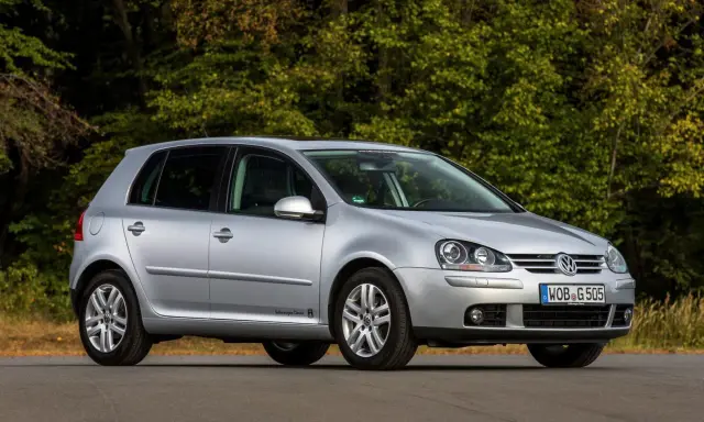 Srebrny Volkswagen Golf V stoi na drodze, otoczony zielenią drzew.