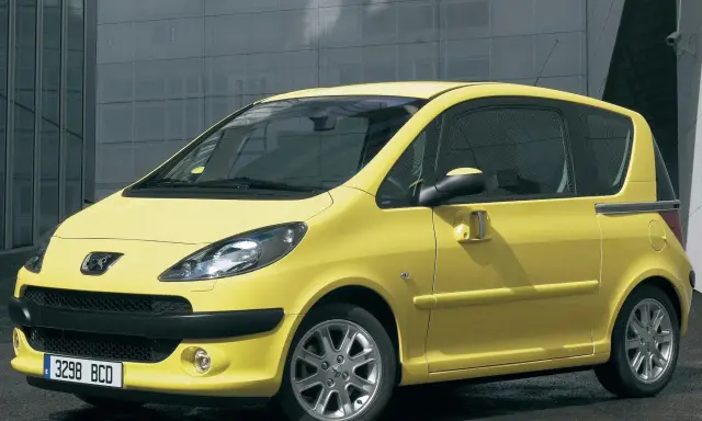 Żółty Peugeot 1007 z przesuwnymi drzwiami stoi przed nowoczesnym budynkiem.