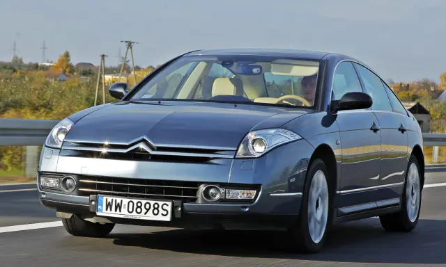 Elegancki Citroën C6 w kolorze granatowym jedzie po drodze. Wnętrze z jasną tapicerką i kierowcą.