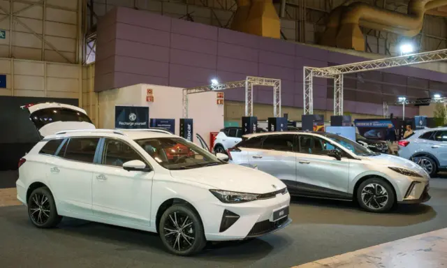 Białe kombi MG5 z otwartą klapą bagażnika i srebrny SUV na wystawie samochodowej.
