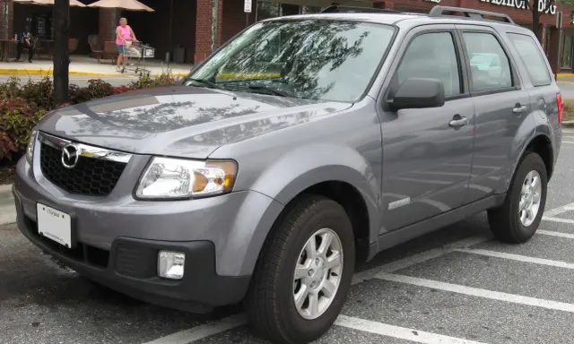 Szary Mazda Tribute zaparkowany na parkingu przed sklepem.