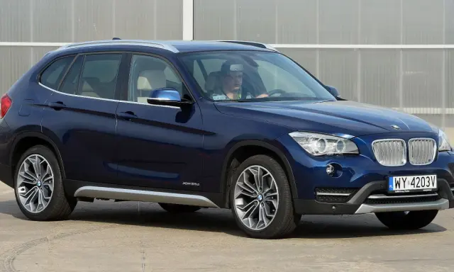 Ciemnoniebieskie BMW X1 E84 z kierowcą za kierownicą, zaparkowane na zewnątrz.