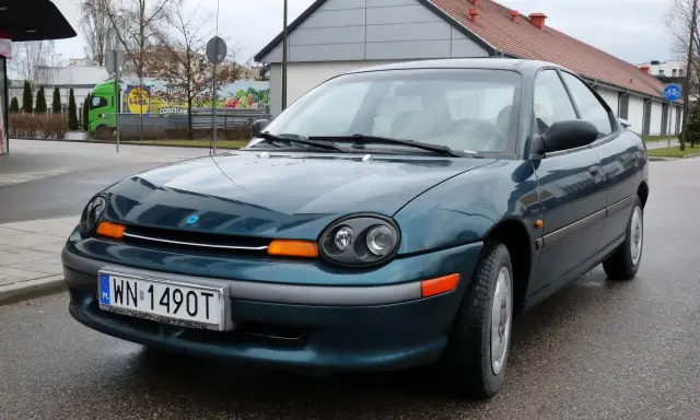 Zielony Dodge Neon z tablicą rejestracyjną WN 1490T stoi na mokrej drodze przed budynkiem.