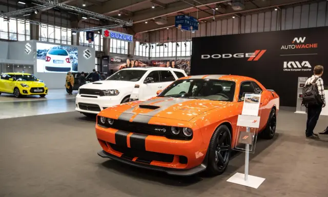 Pomarańczowy Dodge Challenger Hellcat z szarymi pasami na masce, obok białego SUV-a Dodge Durango.