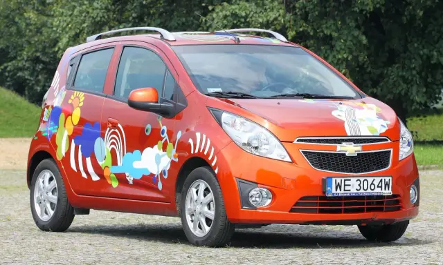 Pomarańczowy Chevrolet Spark z kolorowymi, abstrakcyjnymi wzorami na karoserii.
