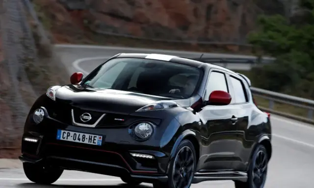 Czarny Nissan Juke Nismo z czerwonymi lusterkami i białym pasem na dachu pędzi po krętej drodze.