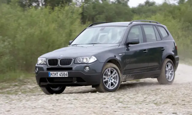 Ciemnoszary BMW X3 2024 na szutrowej drodze, otoczony zielenią.