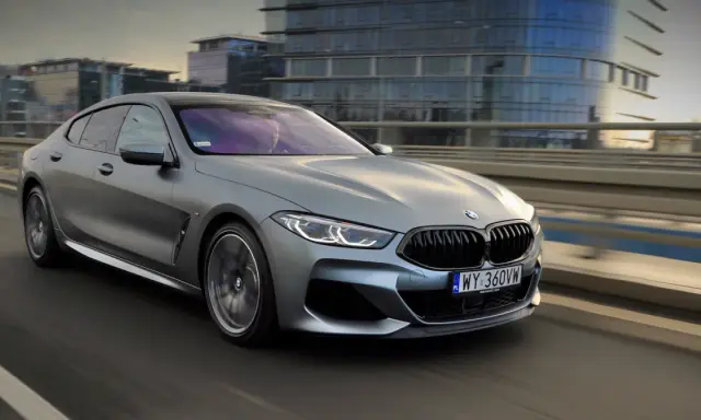 Srebrne BMW M850i sunie po moście, odbijając światła miasta w swoich lśniących szybach.