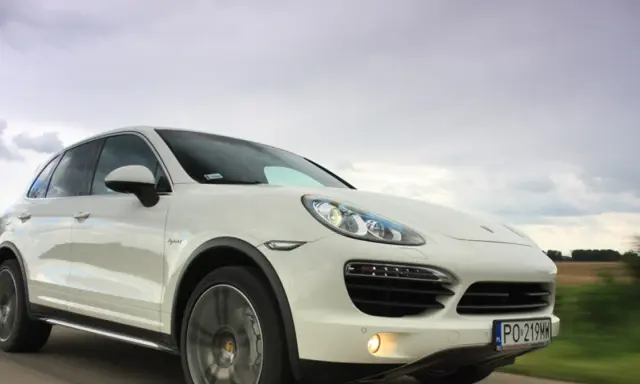 Biały Porsche Cayenne 2025 pędzi po drodze, chmury na niebie sugerują dynamiczną podróż.