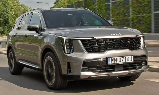 Nowa Kia Sorento w kolorze szarym, z charakterystycznym grillem i nowoczesnymi światłami, pędzi po drodze.